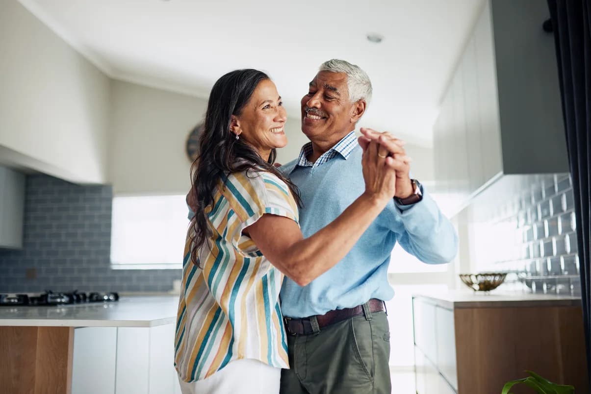 Smiling couple holding hands and dancing together in their kitchen